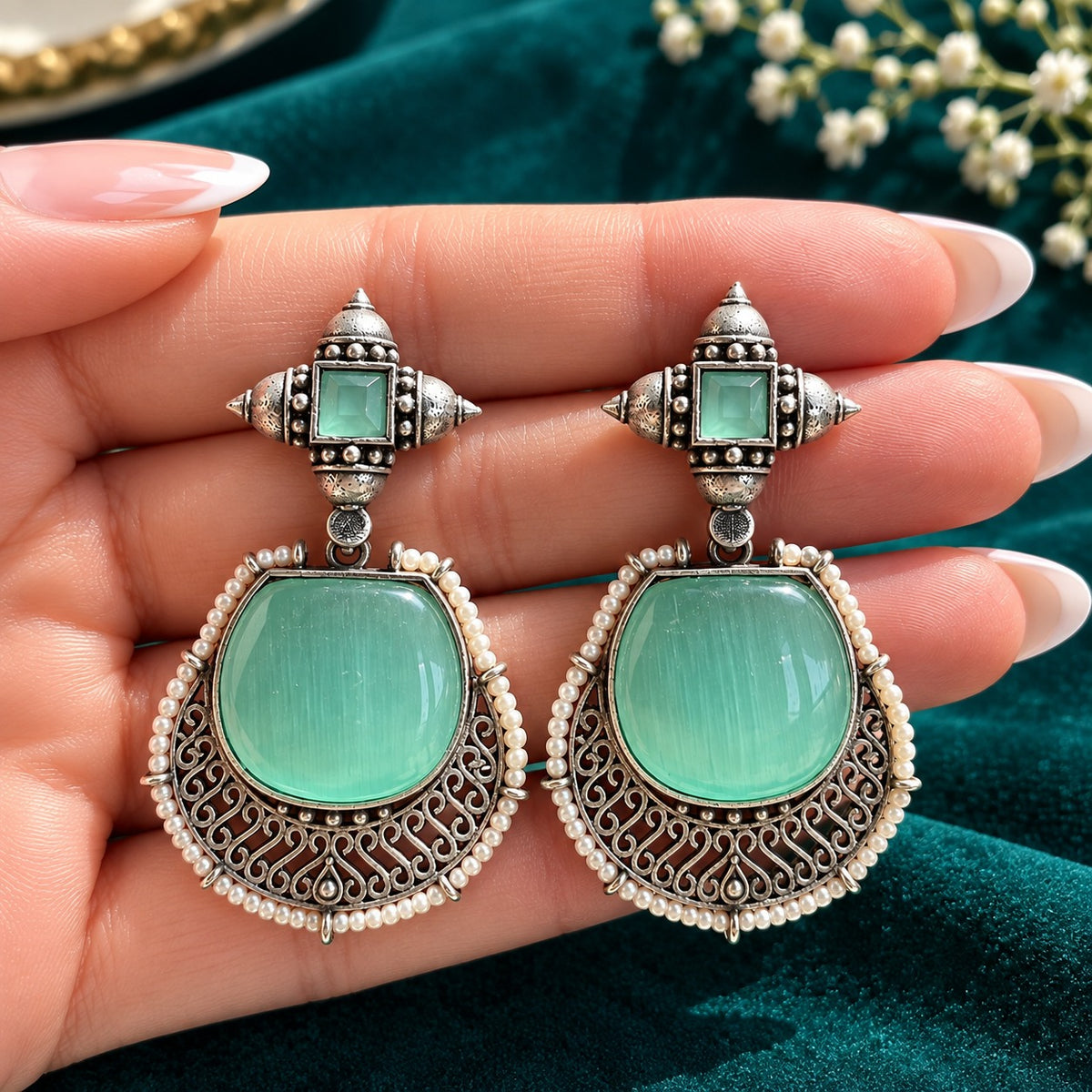 The Ancestral Crest Drops in Mint green with antique silver filigree and pearl detailing on a hand