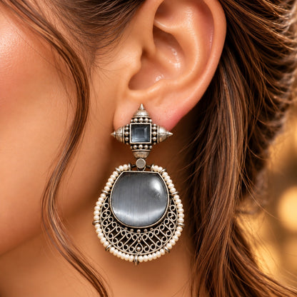 Close-up of antique silver medallion earrings  worn on ear showing the centre stone, filigree and pearl detailing.