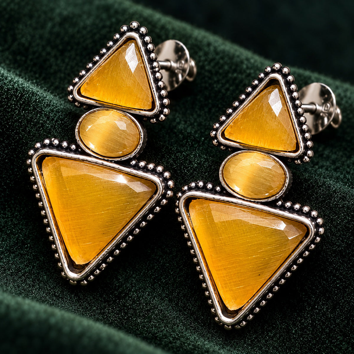 Close up of Amber gold Legacy Trine Earrings featuring two triangular stones, an oval centre and detailed silver-tone edging.