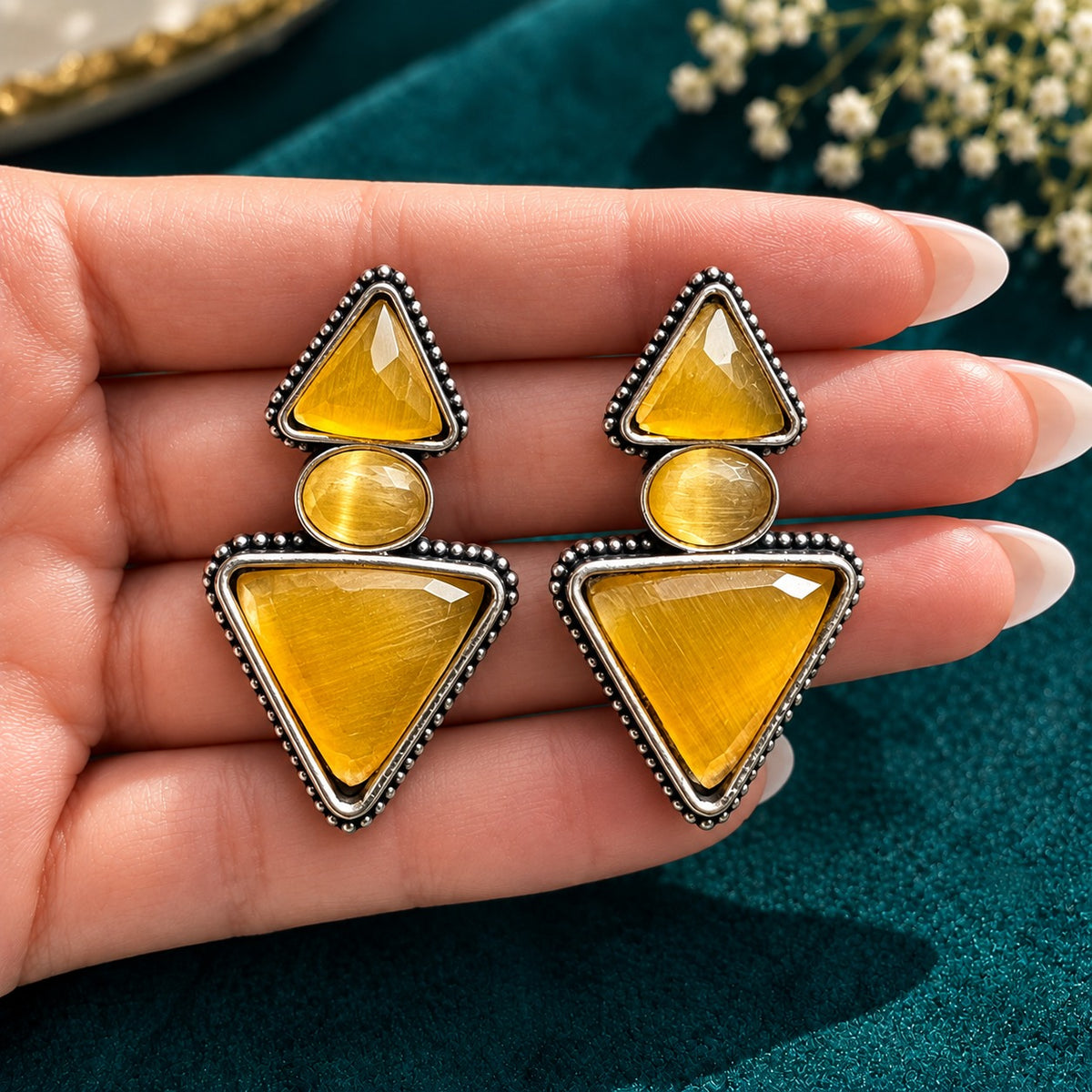 Amber gold Legacy Trine Earrings featuring two triangular stones, an oval centre and detailed silver-tone edging on a hand