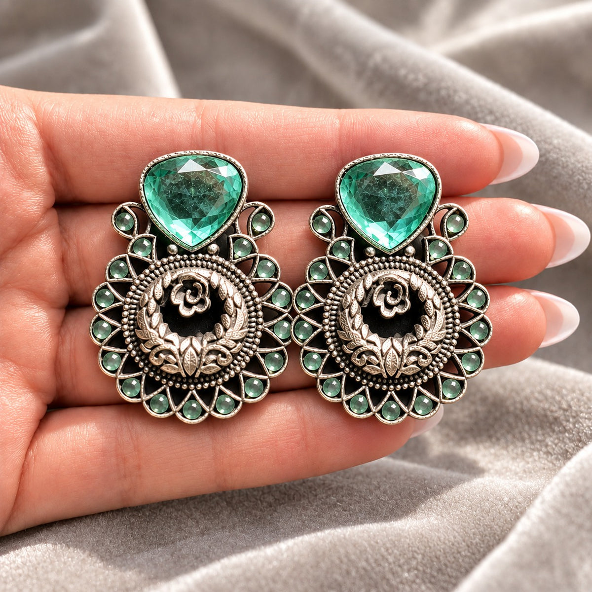 Mint green Courtyard Rose Earrings displayed on a hand, showing their statement size and intricate ornamental detailing.