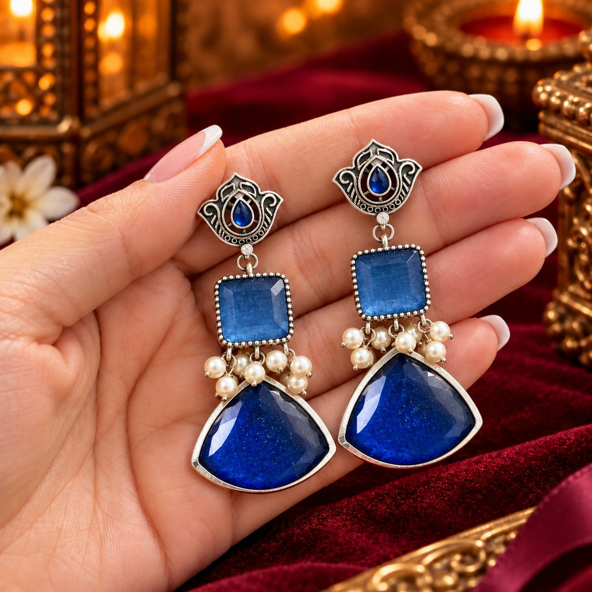 Heirloom Crest Drops in sapphire blue with silver-toned detailing and pearl accents, displayed on hand