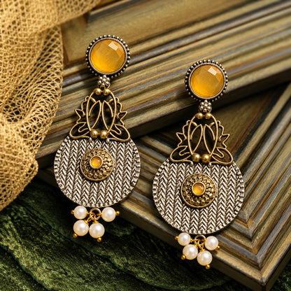 The Loom & Lotus Earrings featuring a textured silver-tone medallion, antique gold lotus detailing, faceted  mustard yellow round stones and pearl drops.