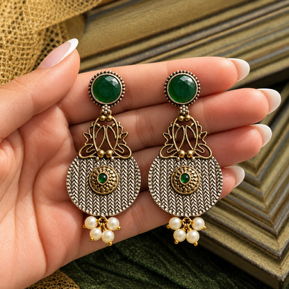 The Loom & Lotus Earrings displayed on a hand, showing their statement length, woven metal texture, mixed-metal detailing and pearl-drop finish.