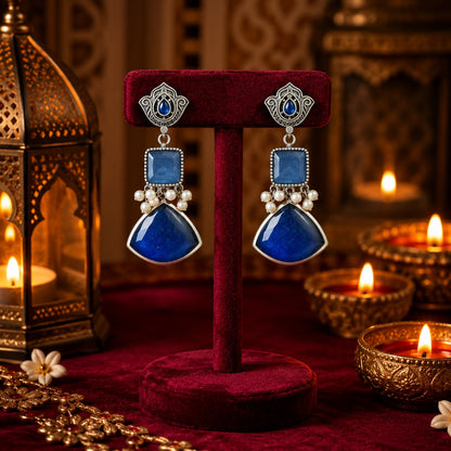 Heirloom Crest Drops in sapphire blue with silver-toned detailing and pearl accents, displayed on rich burgundy velvet.