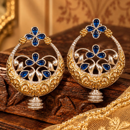 Close-up of statement circular earrings with deep blue teardrop stones, sculpted floral metalwork and jhumka-style drops.