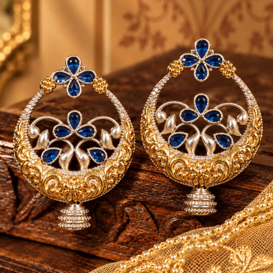 Close-up of statement circular earrings with deep blue teardrop stones, sculpted floral metalwork and jhumka-style drops.