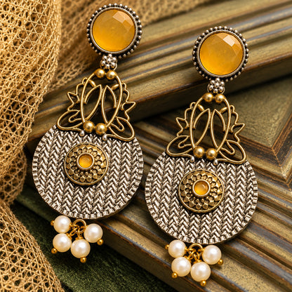 The Loom & Lotus Earrings featuring a textured silver-tone medallion, antique gold lotus detailing, faceted  mustard yellow round stones and pearl drops.