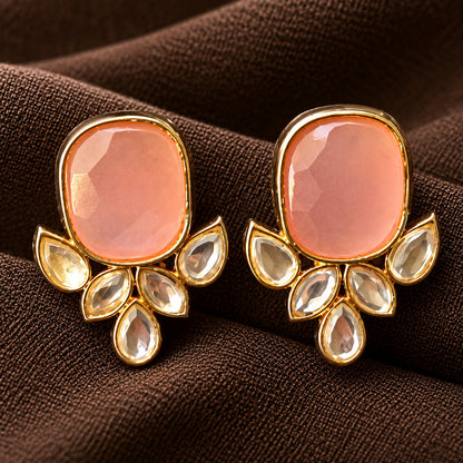 Pair of Legacy Crownleaf Studs with faceted blush pink cushion stones and five clear leaf and teardrop accents, displayed on rich brown fabric.
