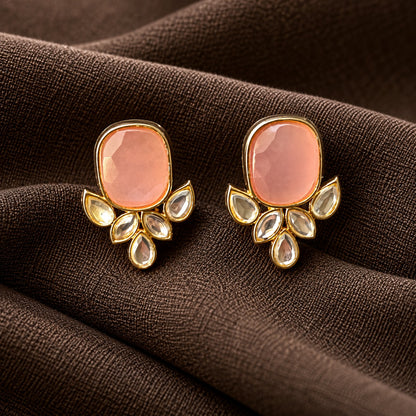 Pair of Legacy Crownleaf Studs with faceted blush pink cushion stones and five clear leaf and teardrop accents, displayed on rich brown fabric.