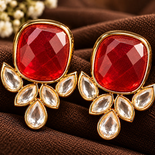 Pair of Legacy Crownleaf Studs with faceted  ruby red cushion stones and five clear leaf and teardrop accents, displayed on rich brown fabric.