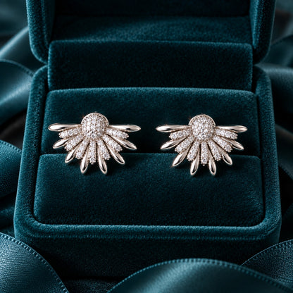 Silver Petal Crest Earrings featuring fan-shaped silver petals, clear zircon detailing and a rounded pavé-style centre against deep teal velvet.