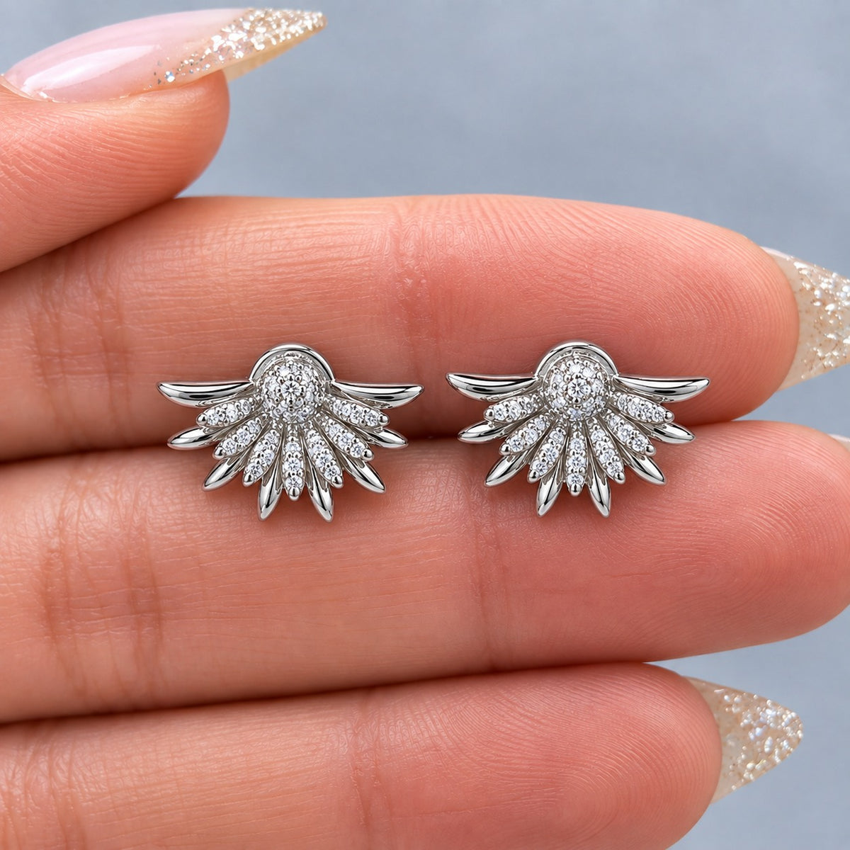 Silver Petal Crest Earrings featuring fan-shaped silver petals, clear zircon detailing and a rounded pavé-style centre held on a hand.