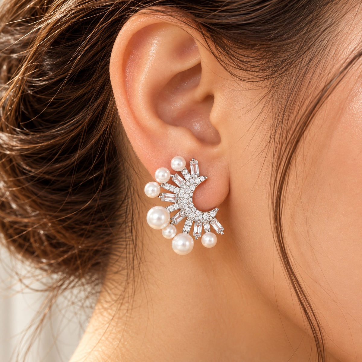 Close-up of a woman wearing silver-tone crescent pearl earrings featuring graduated white pearls and clear zircon stones in a striking statement design.