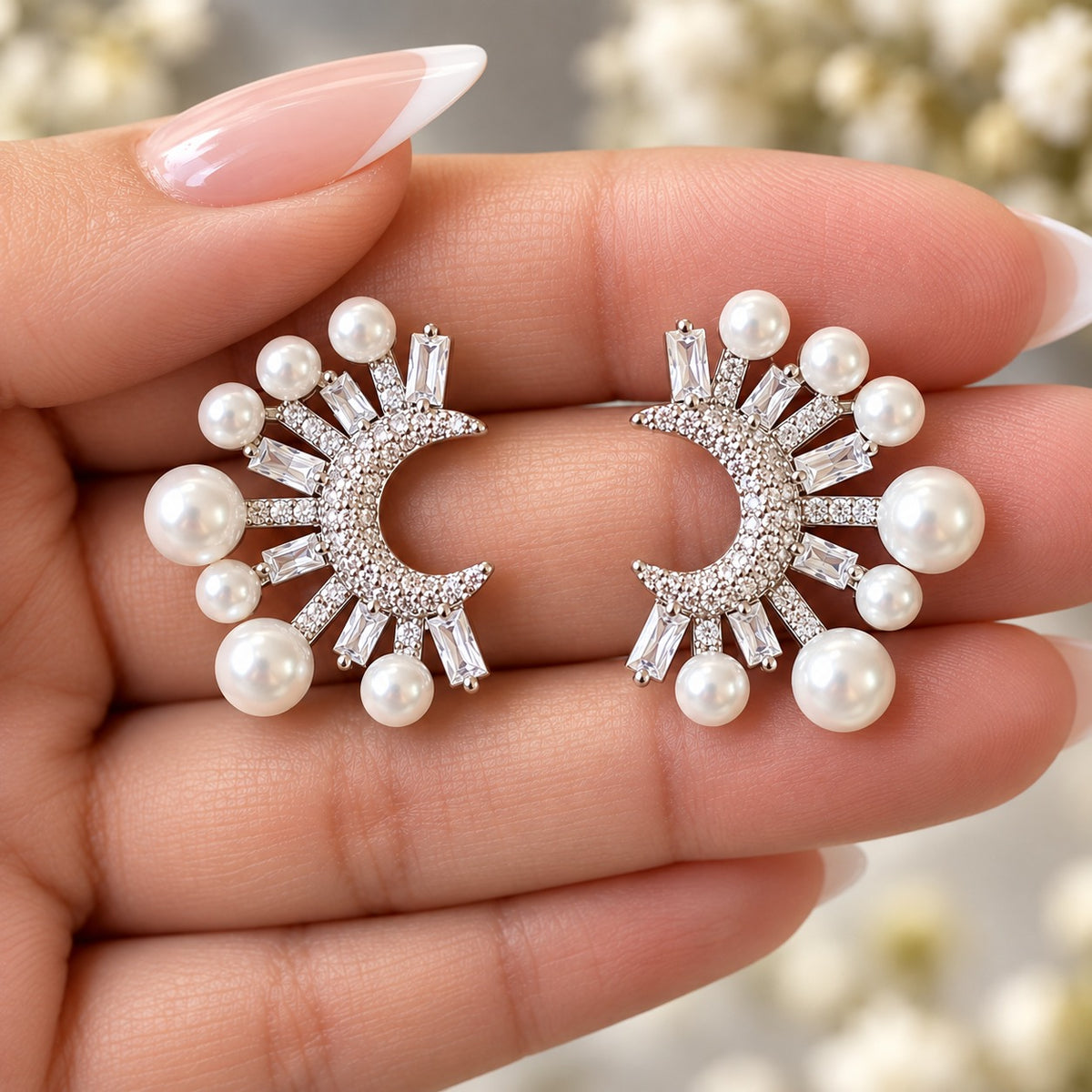 Pair of crescent pearl and baguette zircon earrings displayed against a woman's fingers, highlighting the intricate detailing and overall proportions.