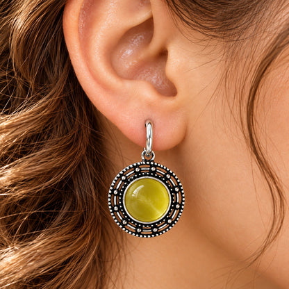 Close-up of a woman wearing olive-lime-green Solstice Medallion Earrings with an antique oxidised silver-tone circular frame