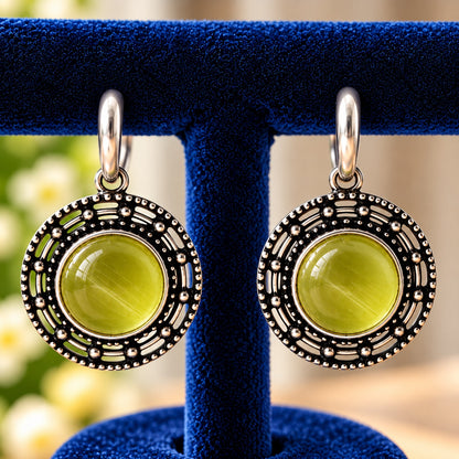 Circular medallion earrings featuring a luminous olive-lime-green centre surrounded by geometric openwork and antique silver-tone detailing.