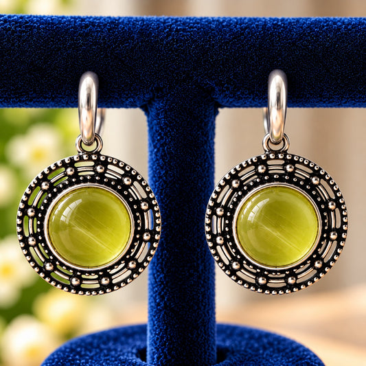 Circular medallion earrings featuring a luminous olive-lime-green centre surrounded by geometric openwork and antique silver-tone detailing.