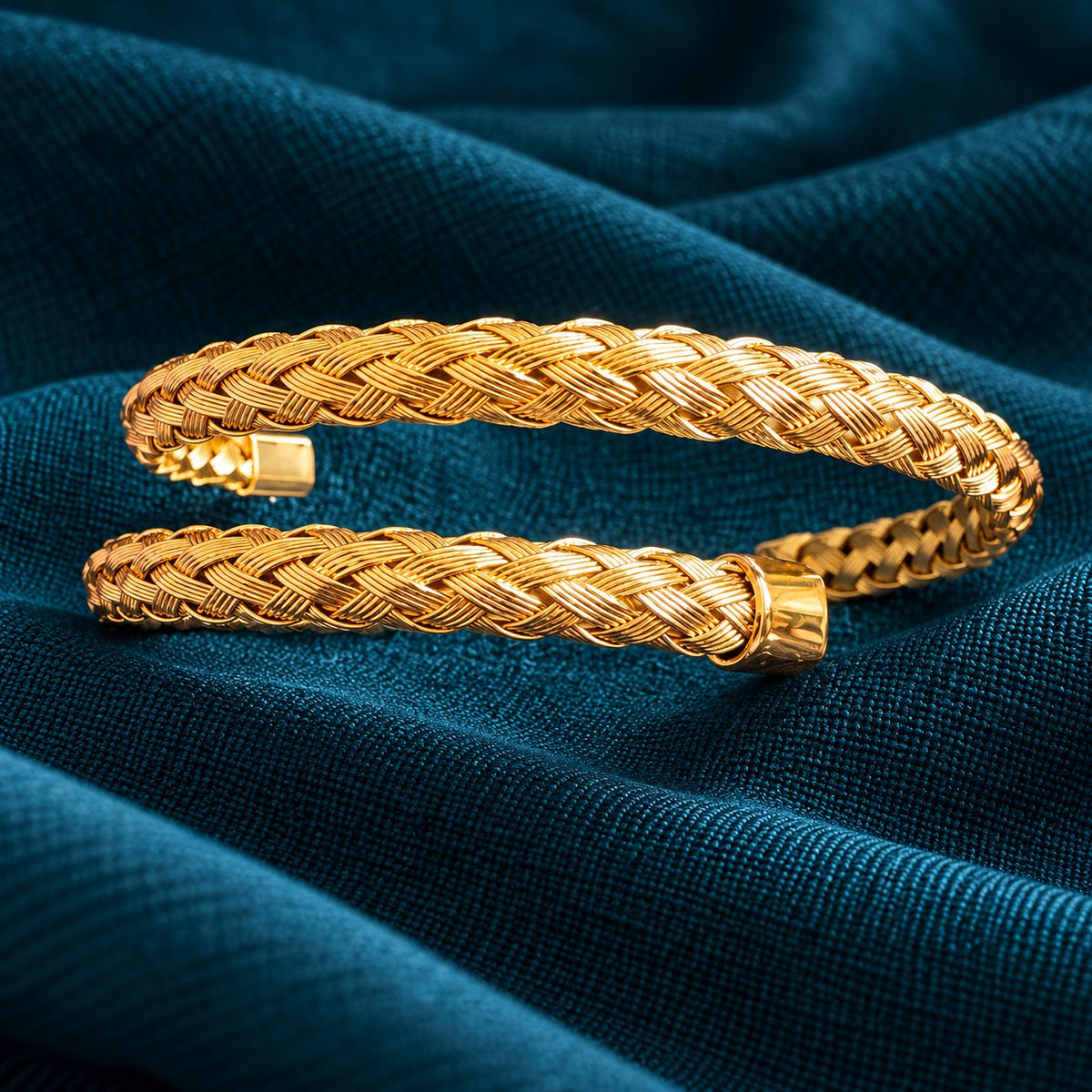 Aurelia Weave Cuff Bracelet featuring intricately braided gold-tone strands, polished end caps, and an open-cuff design on deep teal fabric.