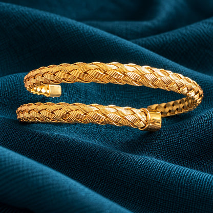 Aurelia Weave Cuff Bracelet featuring intricately braided gold-tone strands, polished end caps, and an open-cuff design on deep teal fabric.