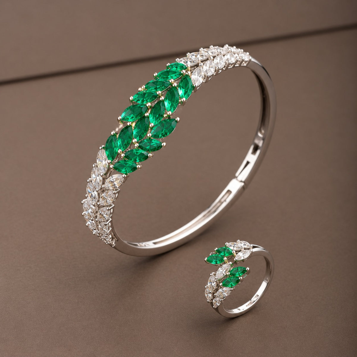 Emerald green and clear zircon bracelet and ring set featuring a silver-tone leaf-inspired design on a taupe background.