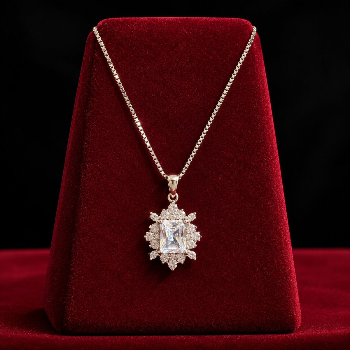 Regent Radiance Zircon Pendant featuring a rectangular-cut clear zircon centre stone surrounded by intricate round and marquise-cut zircon accents, displayed on a rich burgundy velvet stand