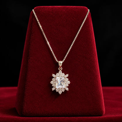 Regent Radiance Zircon Pendant featuring a rectangular-cut clear zircon centre stone surrounded by intricate round and marquise-cut zircon accents, displayed on a rich burgundy velvet stand