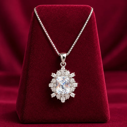 Regent Radiance Zircon Pendant featuring a rectangular-cut clear zircon centre stone surrounded by intricate round and marquise-cut zircon accents, displayed on a rich burgundy velvet stand