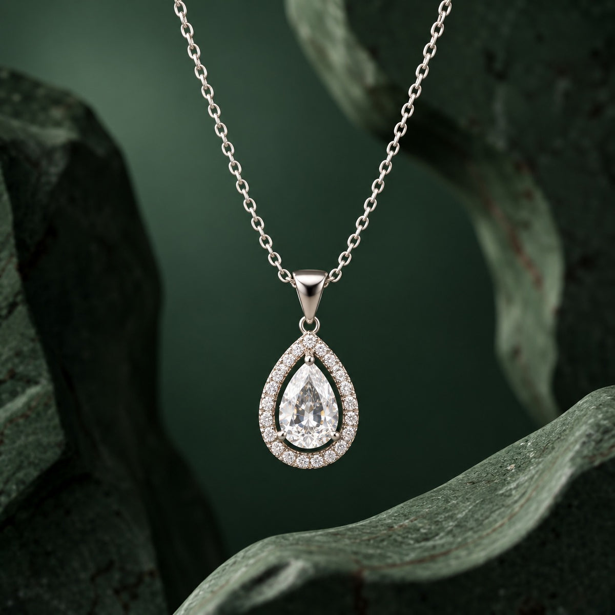 Aurelle Pear Zircon Pendant displayed against a dark green sculptural backdrop, showcasing its teardrop design and clear zircon stones.