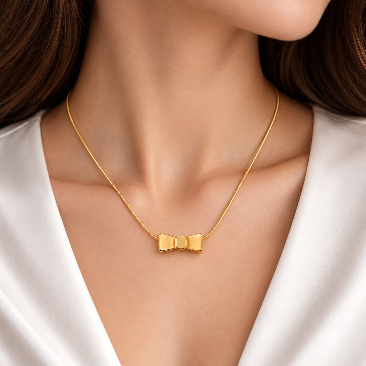 Woman wearing a delicate gold-tone necklace featuring a polished bow-shaped pendant with a rounded central knot, styled with a white outfit