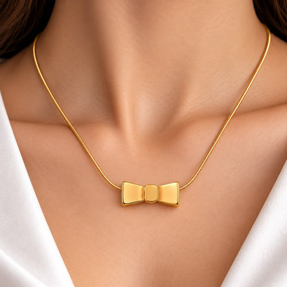 Woman wearing a delicate gold-tone necklace featuring a polished bow-shaped pendant with a rounded central knot, styled with a white outfit