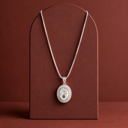 Silver-tone Aurelle Oval Zircon Pendant with a coordinating chain, showcasing its oval-cut crystal-clear centre stone and double zircon border on a premium terracotta jewellery display.