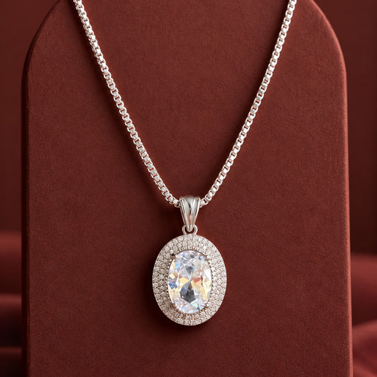 Aurelle Oval Zircon Pendant featuring a large oval-cut clear zircon gemstone surrounded by a double border of tiny zircon stones, displayed on a rich terracotta jewellery stand