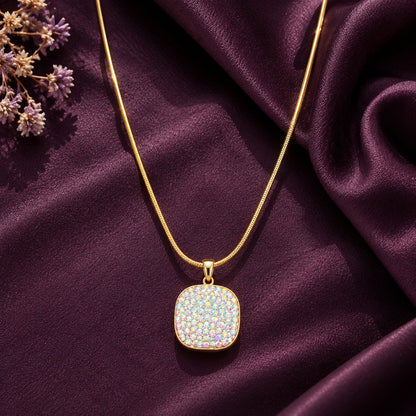 Gold-tone mosaic pendant featuring shimmering multicoloured pastel stones, displayed on rich plum satin fabric with delicate floral accents.