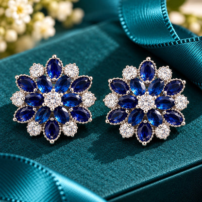 Vespera Bloom Earrings in sapphire blue, featuring layered marquise-cut gemstones, clear zircon accents and polished silver-tone settings, displayed on a teal jewellery box.
