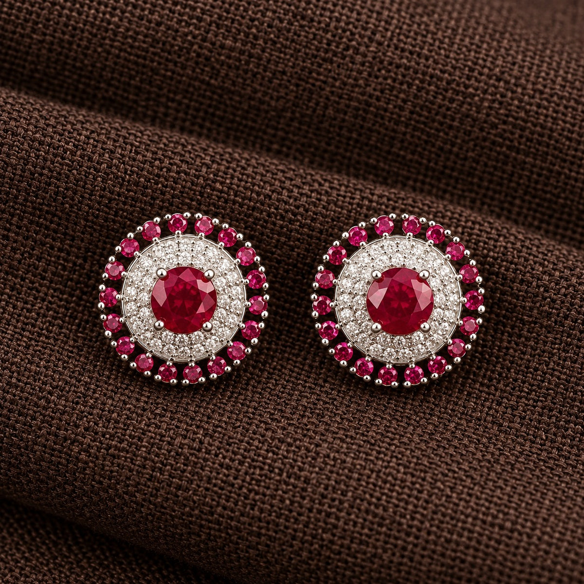 Regent Medallion Studs featuring a faceted raspberry pink centre stone, delicate clear zircon detailing, and an outer circle of ruby red gemstones in a polished silver-tone setting.