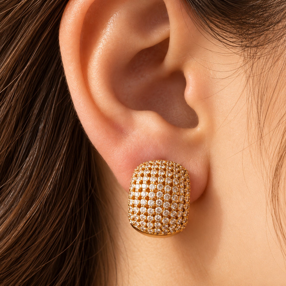 Close-up of a woman's ear wearing Gilded Mosaic Huggie Earrings, highlighting the gold finish, intricate zircon detailing and bold curved silhouette.