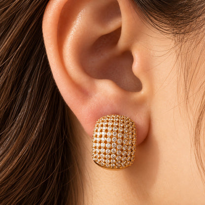 Close-up of a woman's ear wearing Gilded Mosaic Huggie Earrings, highlighting the gold finish, intricate zircon detailing and bold curved silhouette.