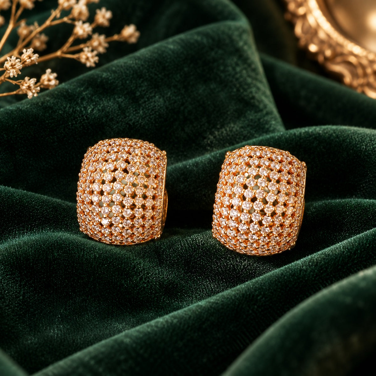 Gilded Mosaic Huggie Earrings in polished gold tone, featuring a curved rectangular design covered with clear zircon stones, displayed on deep forest green velvet.