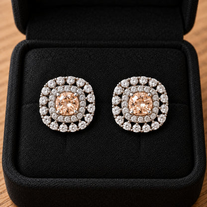 Close-up of silver-tone cushion-shaped stud earrings featuring soft champagne faceted centre stones and intricate double-halo zircon detailing.