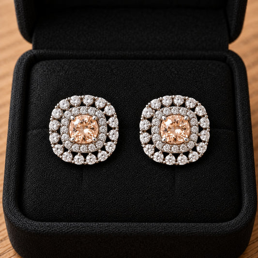Close-up of silver-tone cushion-shaped stud earrings featuring soft champagne faceted centre stones and intricate double-halo zircon detailing.
