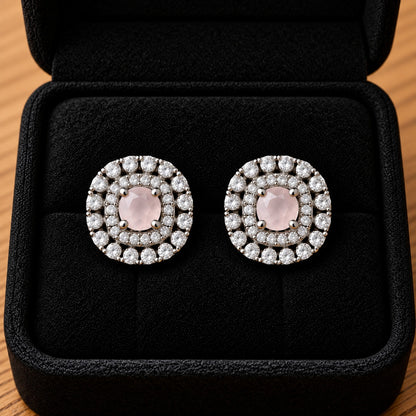 Close-up of silver-tone cushion-shaped stud earrings featuring soft pale pink faceted centre stones and intricate double-halo zircon detailing.