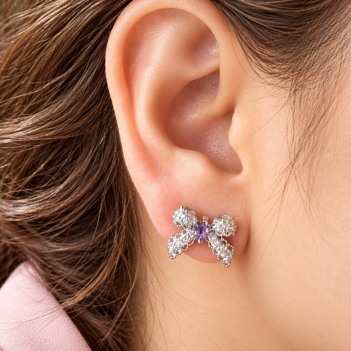 Close-up of a woman's ear wearing an Amorette Bow Stud with an amethyst purple centre stone and delicate clear zircon embellishments.