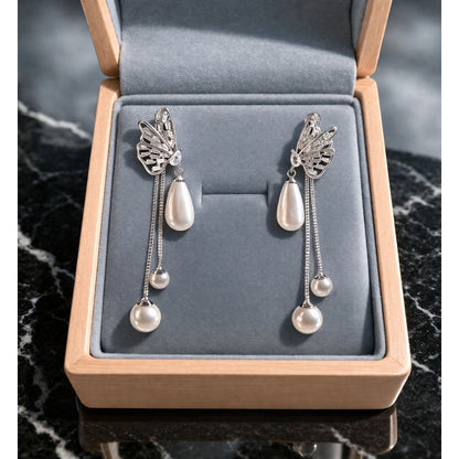 Silver butterfly pearl drop earrings displayed in grey velvet jewelry box on marble surface