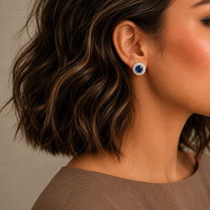 Royal blue halo gemstone stud earrings worn on model featuring sparkling crystal halo in silver-tone finish.