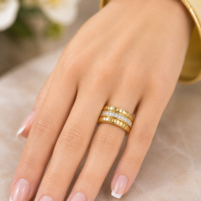 Gold-tone stainless steel ridged band with a crystal center strip worn on a hand against a polished marble vanity with soft floral décor