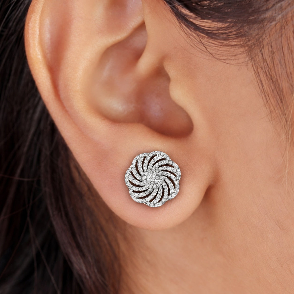 Close-up of a silver circular zircon stud earring with an intricate swirling design worn on the ear.