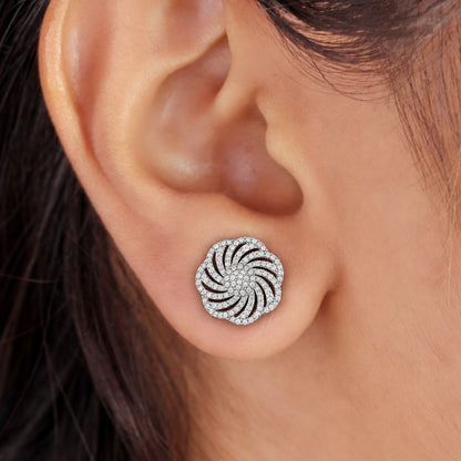 Close-up of a silver circular zircon stud earring with an intricate swirling design worn on the ear.