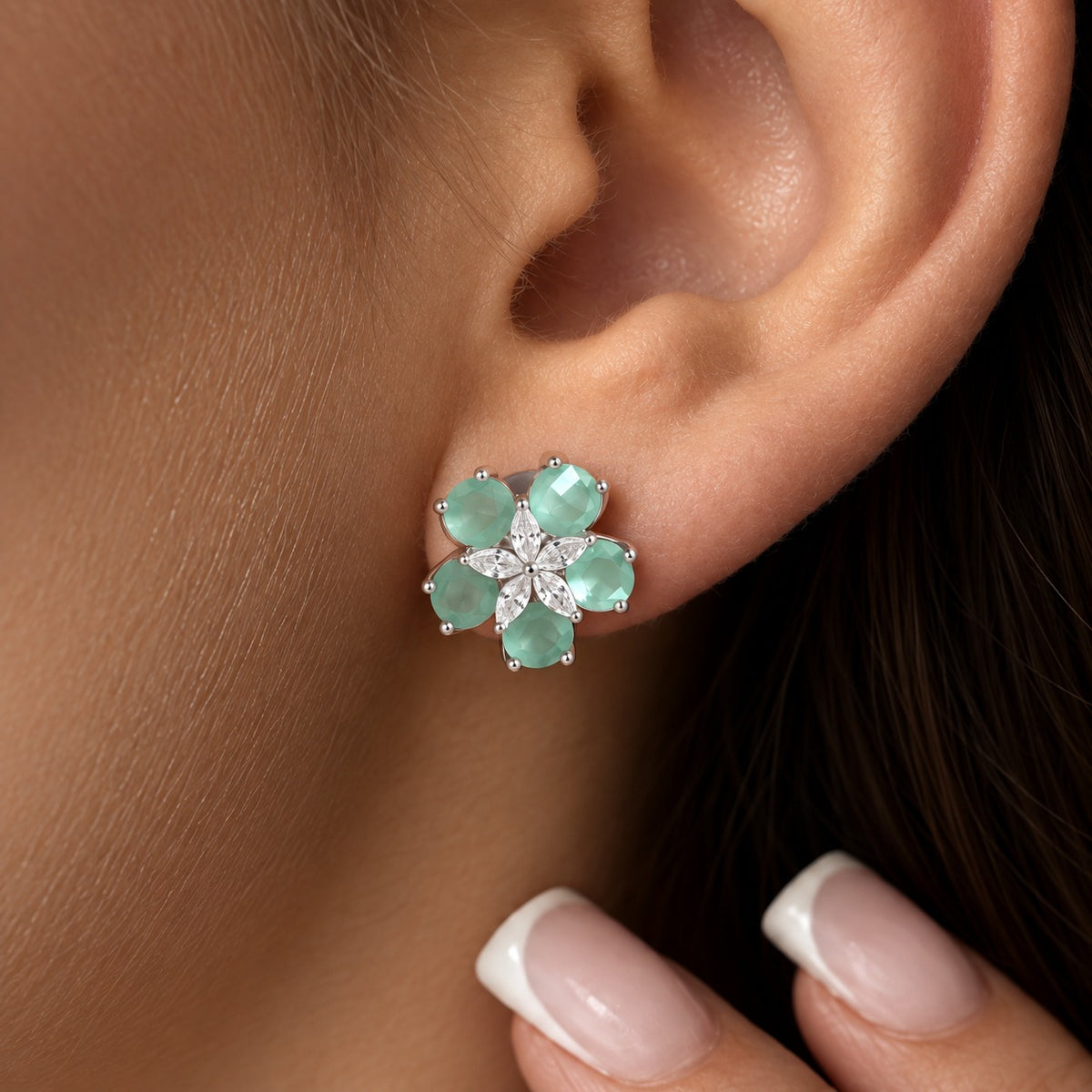 Close-up of Fivefold Bloom Stud worn on the ear, featuring five aqua blue faceted stones surrounding a delicate five-petal clear crystal centre in silver-tone metal.