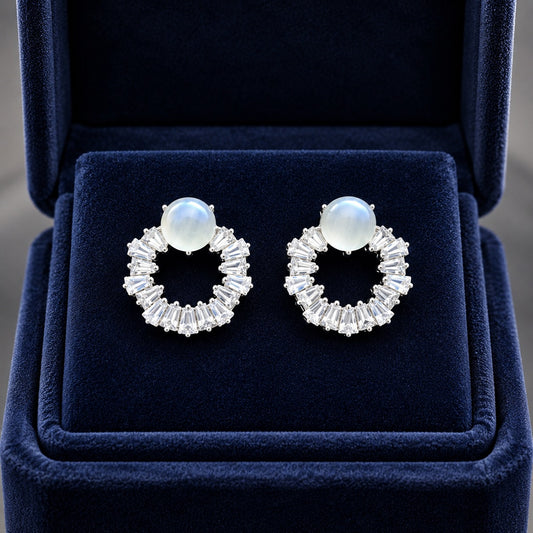 Moonstone halo crystal stud earrings displayed in a premium navy blue velvet jewelry box with sparkling baguette-cut stones and silver-tone finish.